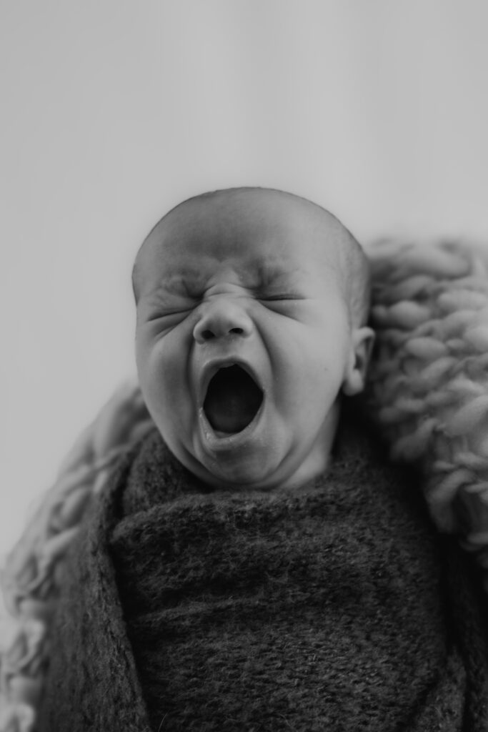 newborn baby boy yawning while wrapped and laying on blanket