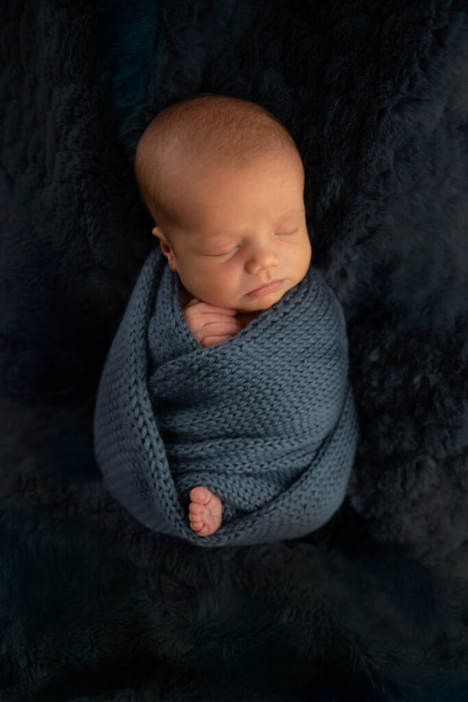 newborn baby boy wrapped in knit blue sleeping on fur