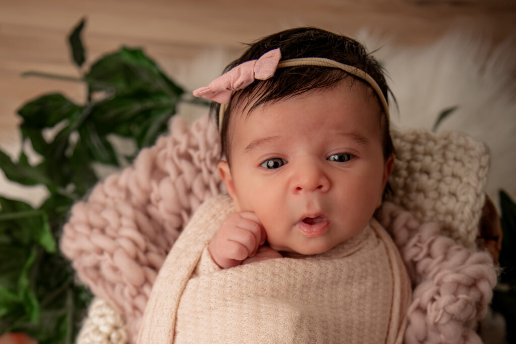 awake baby girl wearing pink bow in cozy basket