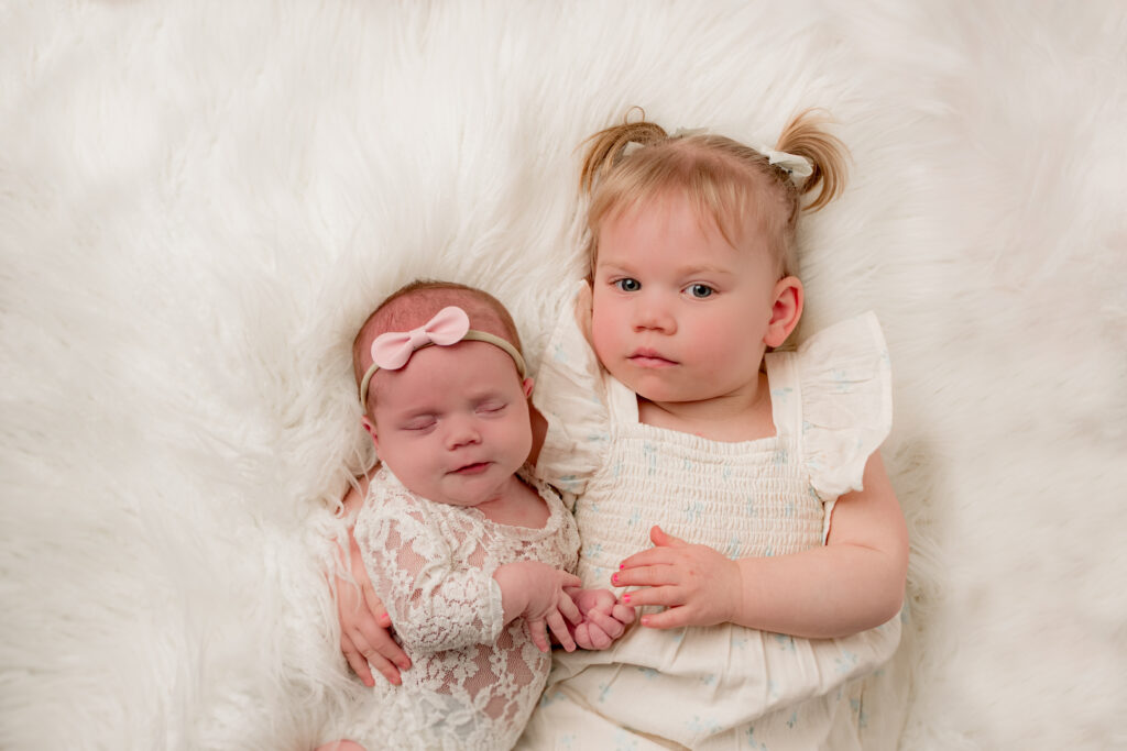 newborn girl sleeping by big sister on white fluffy rug