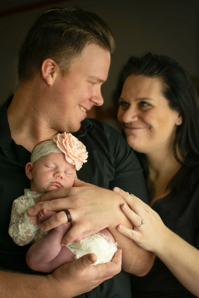 new family of three smiling and holding baby with bow