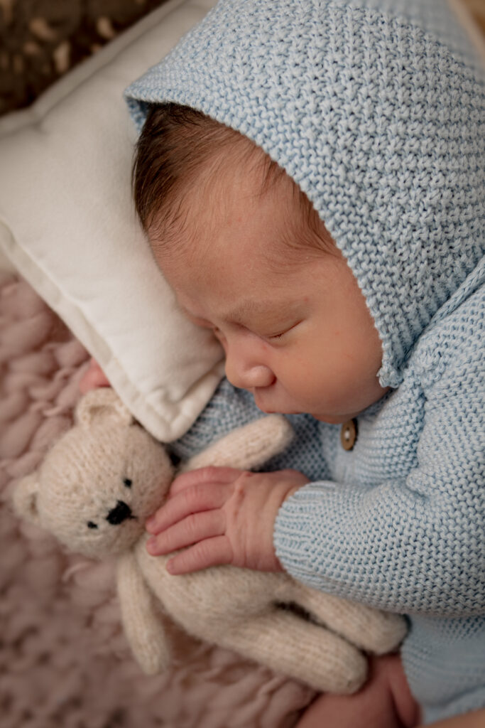 newborn baby boy in blue outfit holding little teddy bear