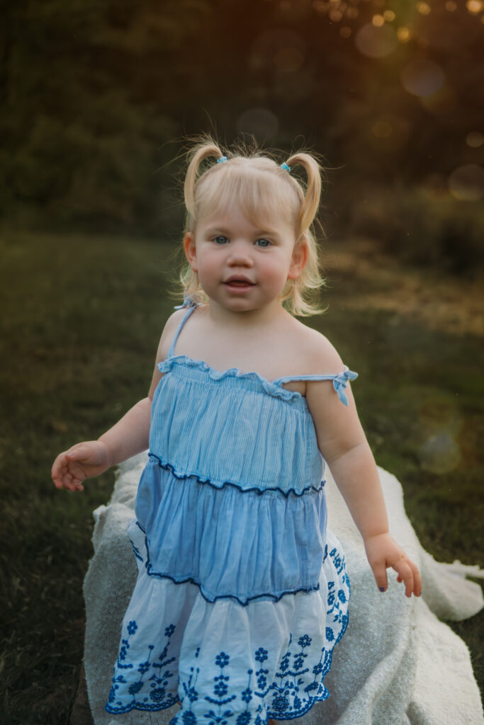 little girl with blue dress smiling as the sun is setting behind her