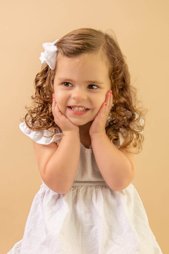smiling girl hands on cheeks curly hair with white bow pageant photography pictures