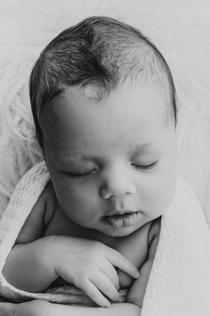 black and white picture of newborn baby girl with swirl hair and long eyelashes